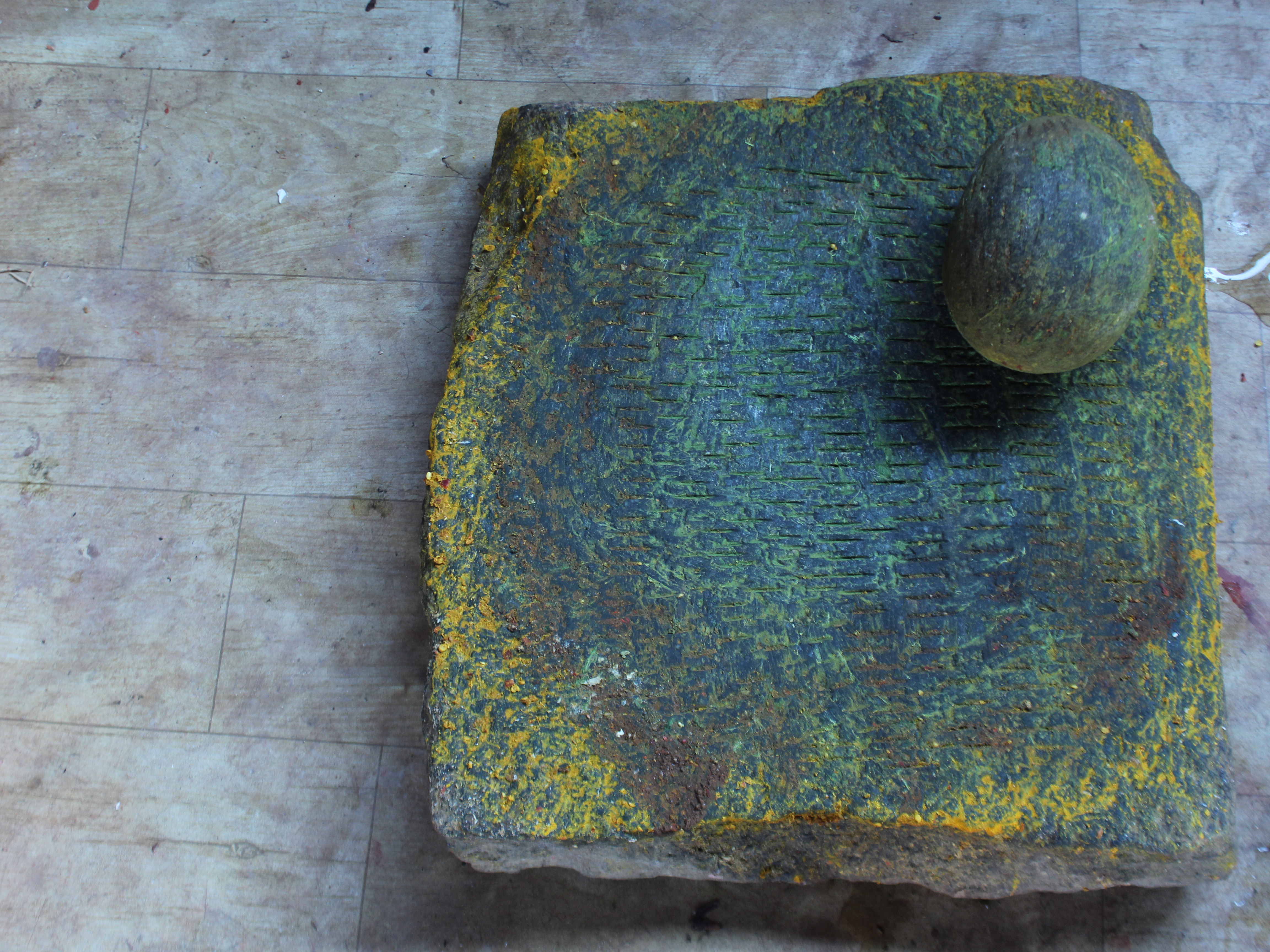 Top view of a textured stone slab with a round stone on one corner, set against a wooden floor.